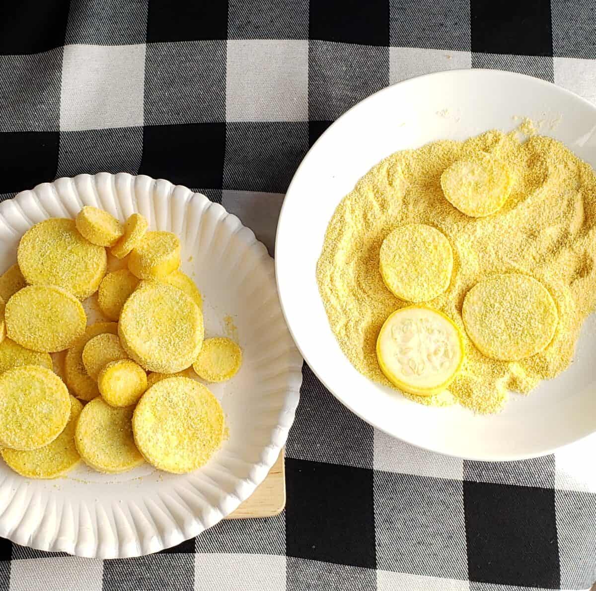 Coating yellow squash in cornmeal on white paper plates on black and white checkered fabric