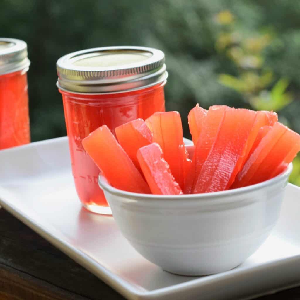 Red pickle sticks in white bowl with sealed jar of pickles to the left