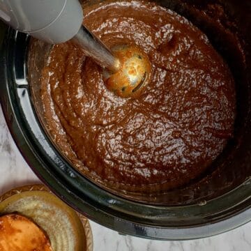 Overhead view of fig jam in a slow cooker with immersion blender in the crock.
