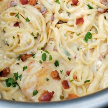 Close up of creamy chicken fettuccine mixture sprinkled with bacon and parsley.