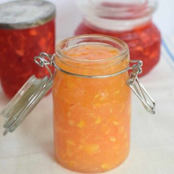 peach marmalade in old fashioned canning jar opened with two strawberry jam jars in background