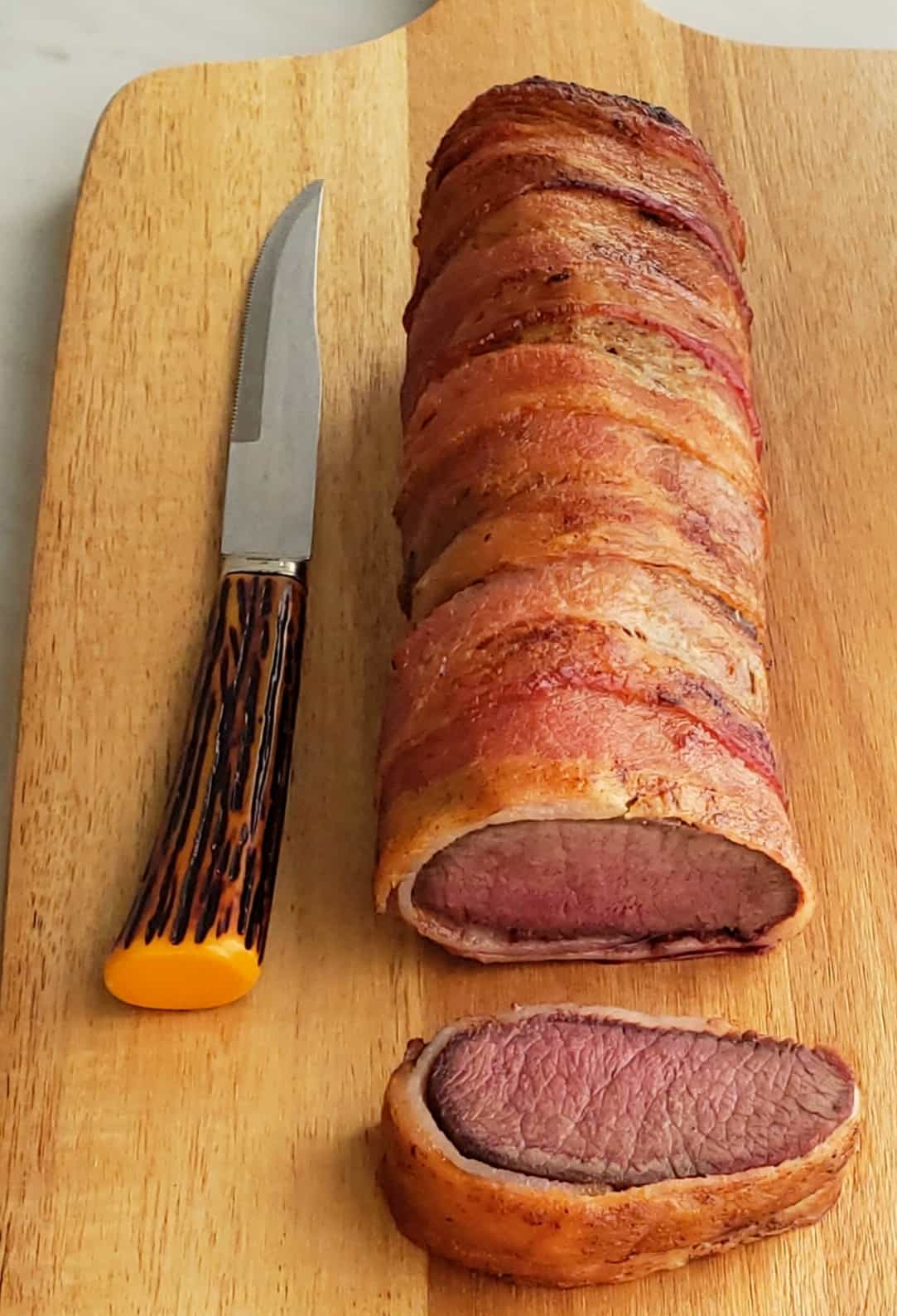 venison roast wrapped in bacon. slice on cutting board