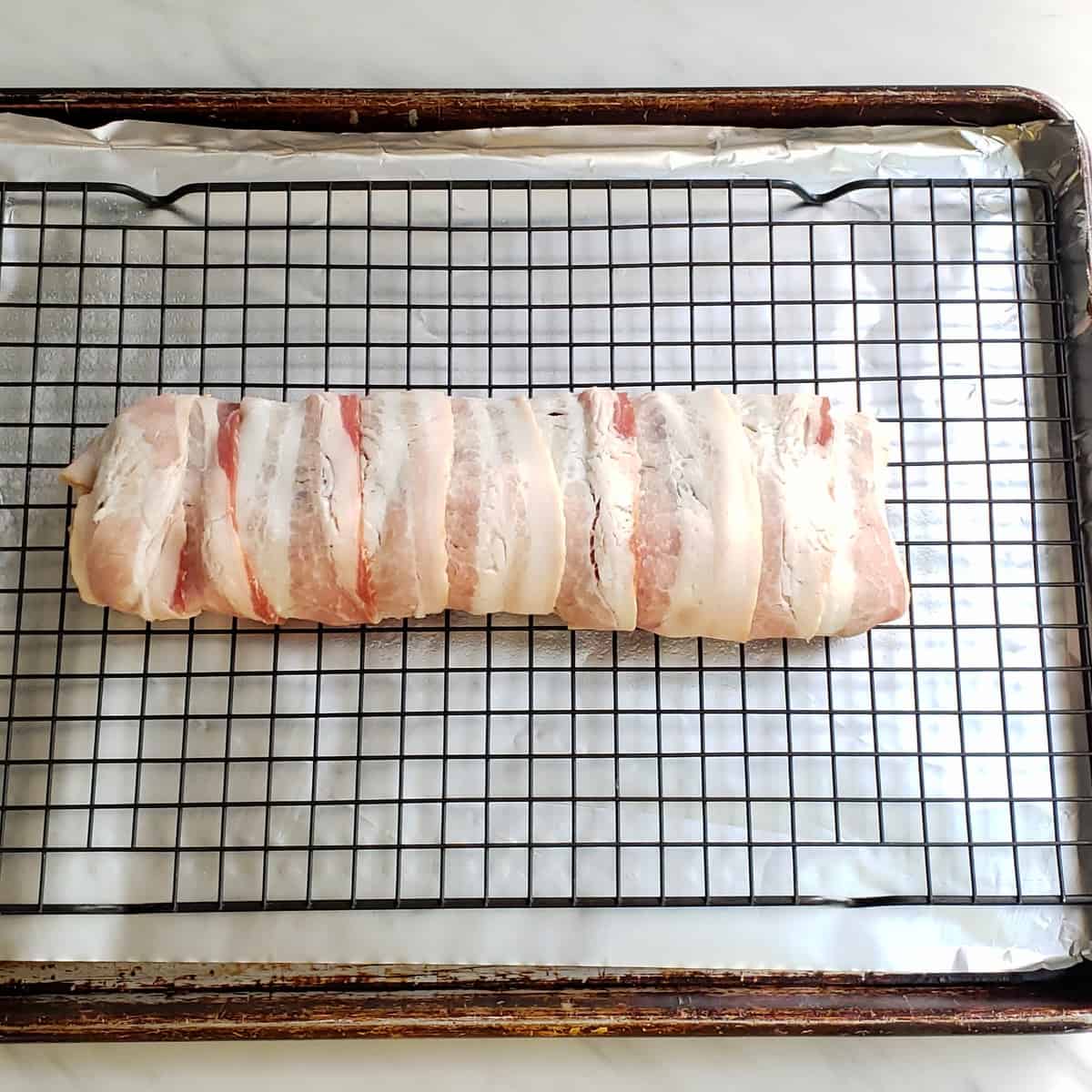 uncooked bacon wrapped venison on wire rack