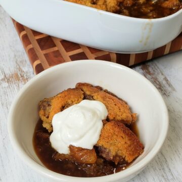 Fig pudding cake with sauce in bottom of white bowl topped with vanilla yogurt