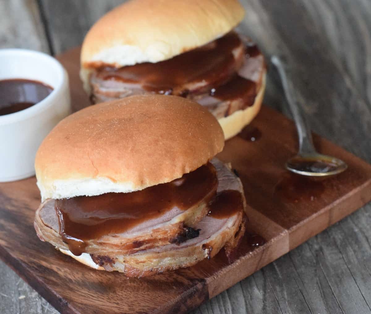 Two venison sliders on wooden cutting board with bbq sauce dripping