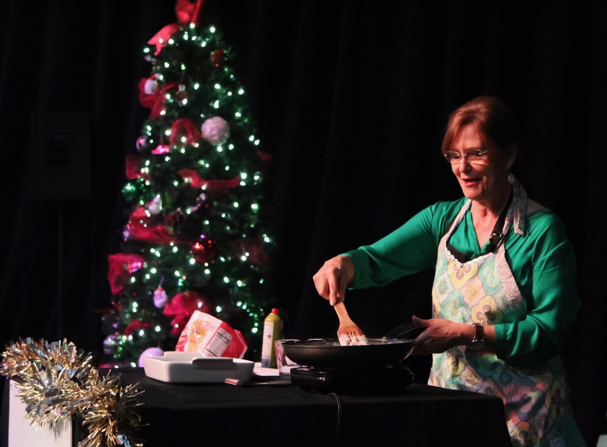 Kathleen Phillips cooking on stage holiday cooking show with christmas tree in background.