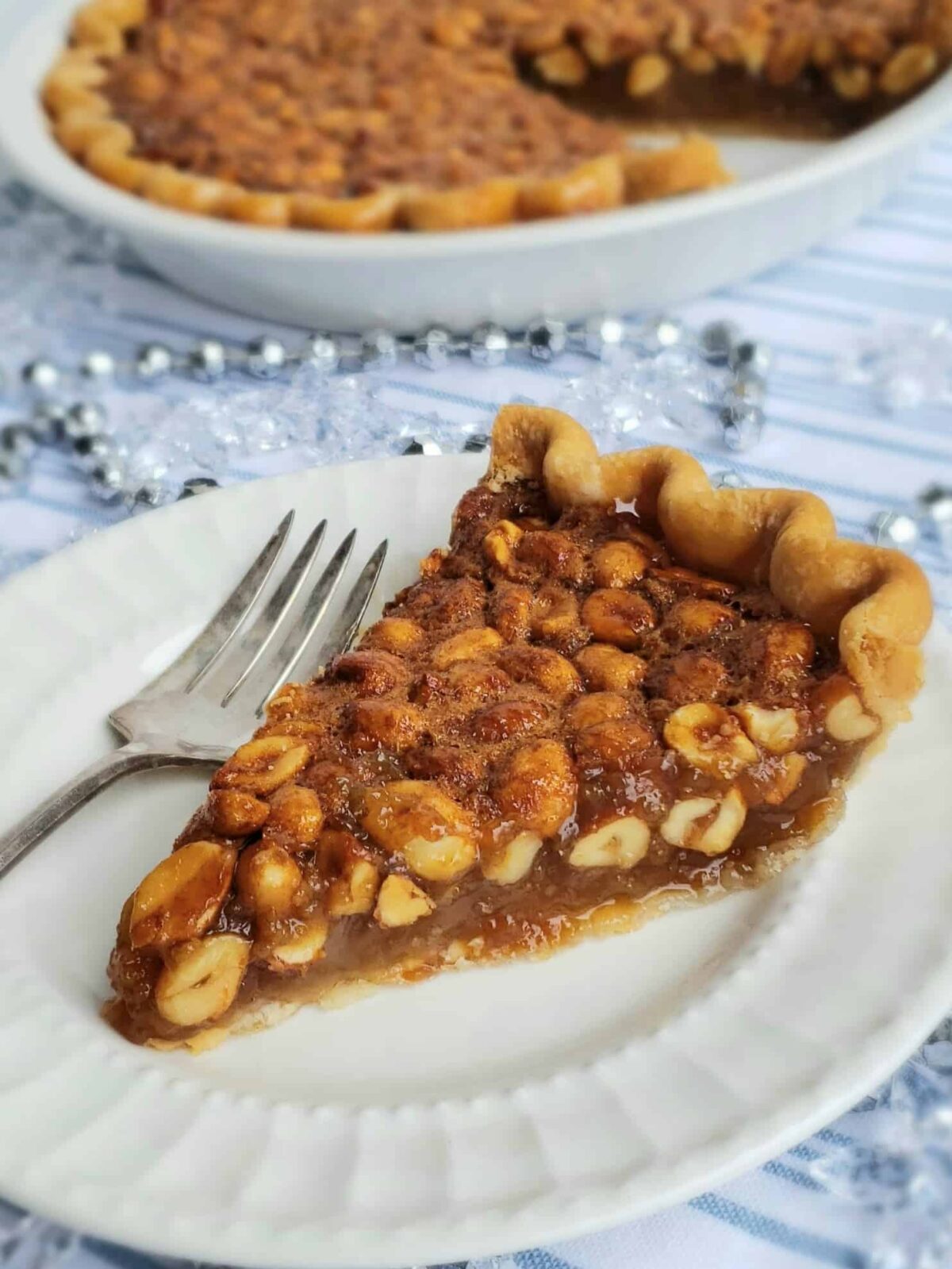 peanut pie slice on white plate with whole pie in background and stack of plates