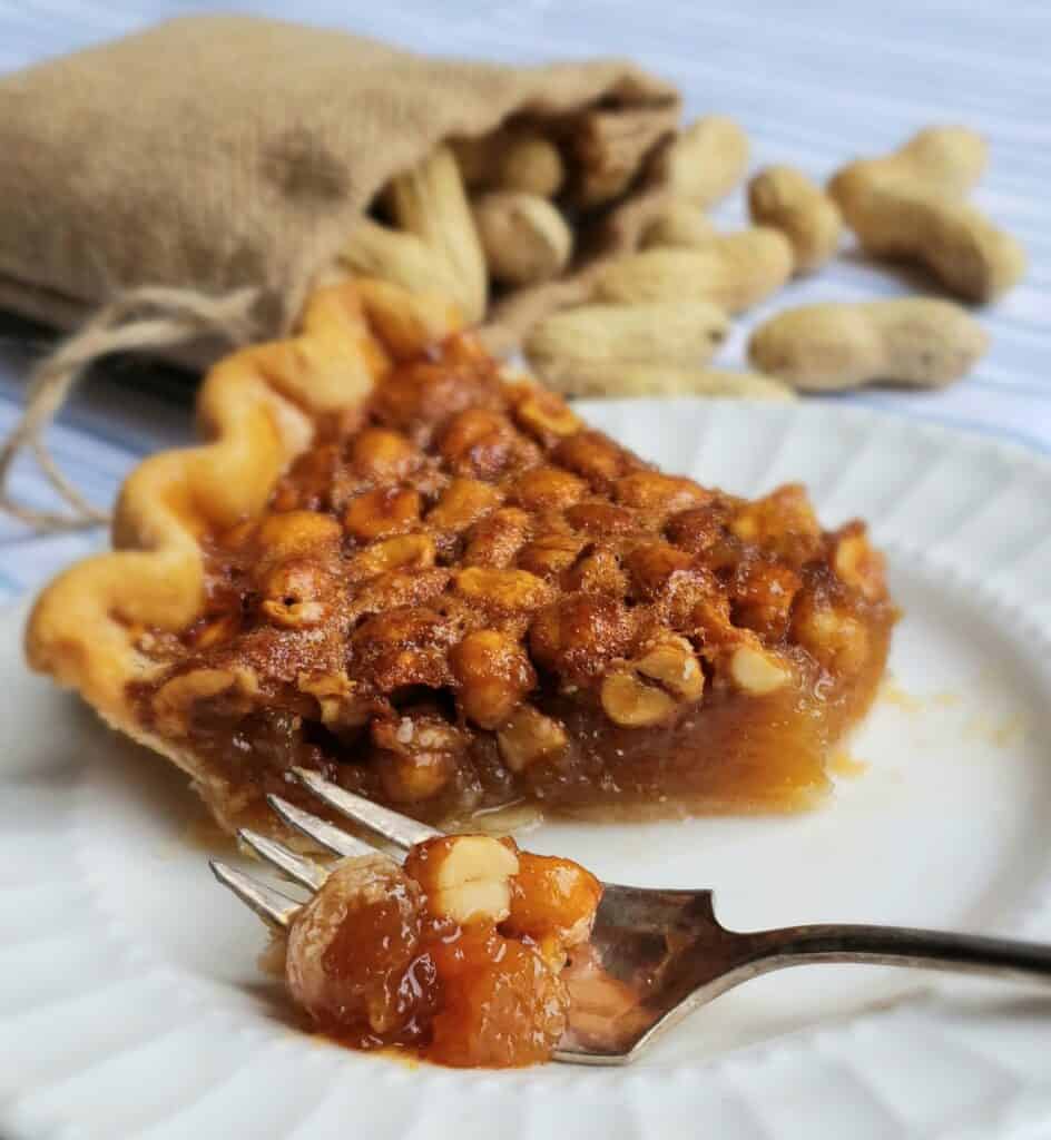 peanut pie with bite cut off on fork on white plate peanuts in a bag