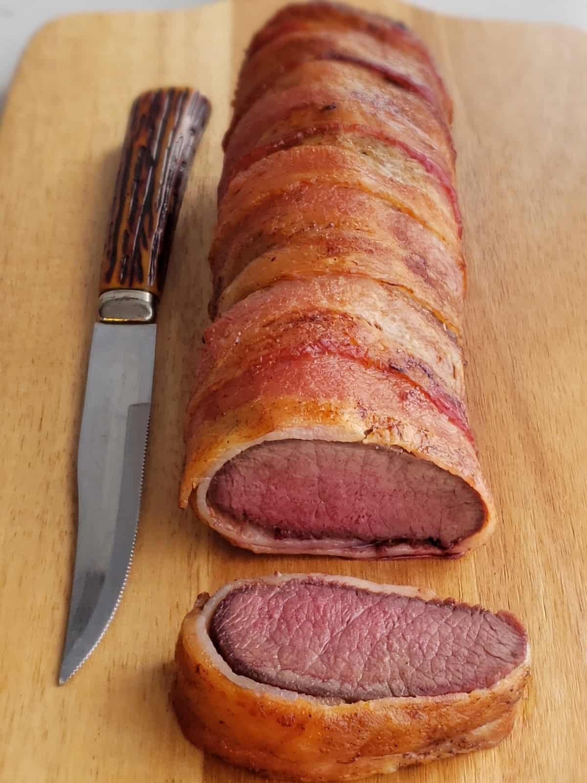 venison roast wrapped in bacon. slice on cutting board