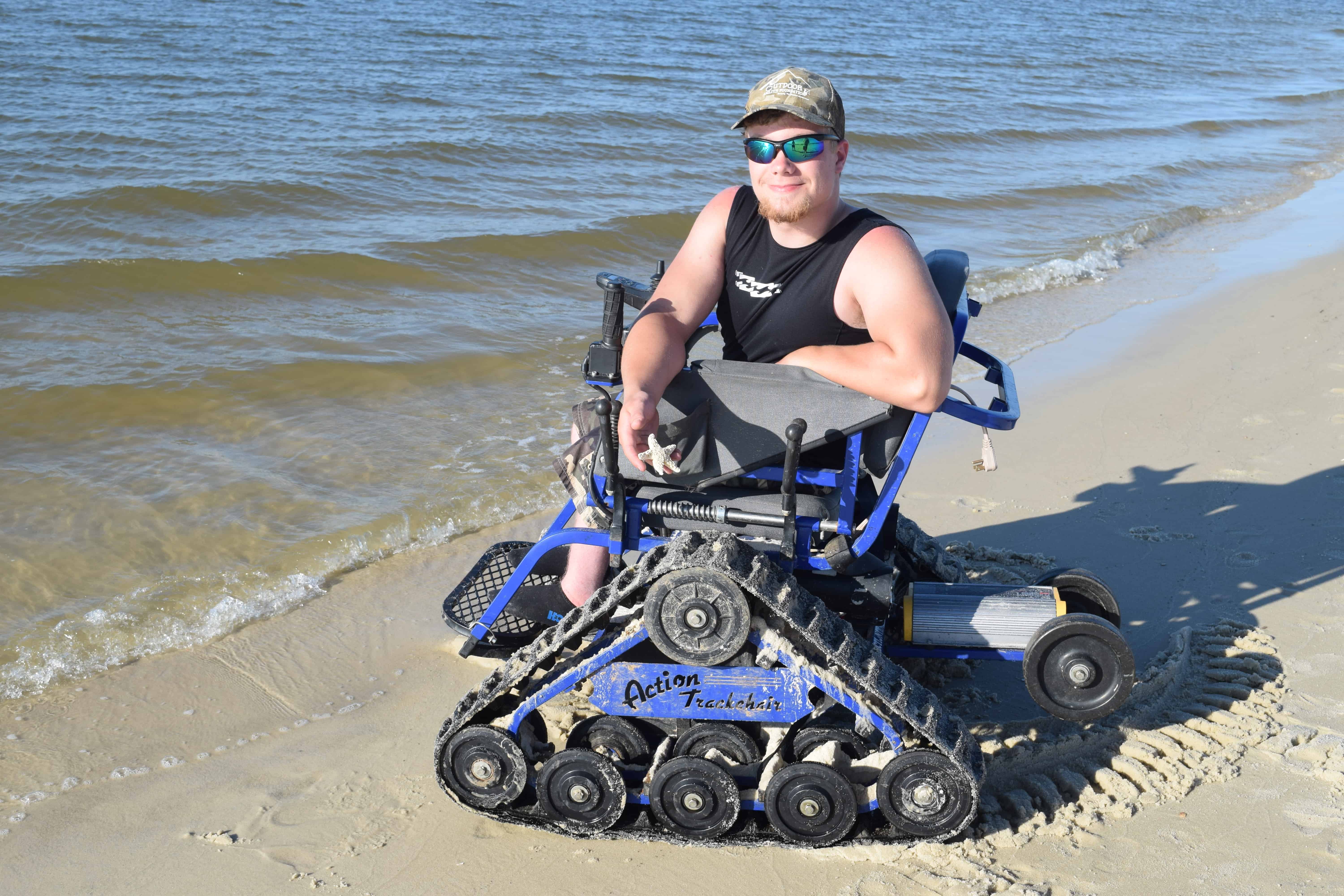 boy in all terrain power wheelchair holding star fish on beach