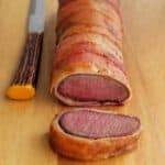 Bacon wrapped venison roast on cutting board. slice cut. steak knife