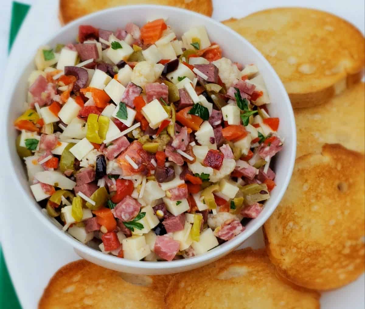 White bowl of Muffuletta Dip surrounded by crostini.