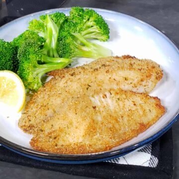 breaded tilapia on blue and white plate with broccoli and lemon
