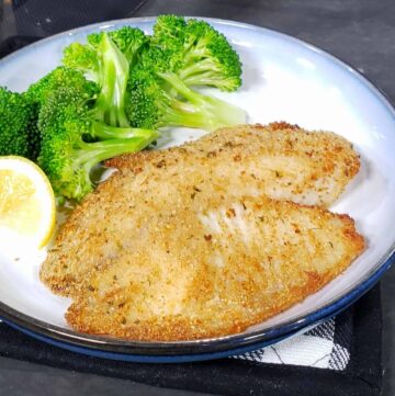 breaded tilapia on blue and white plate with broccoli and lemon