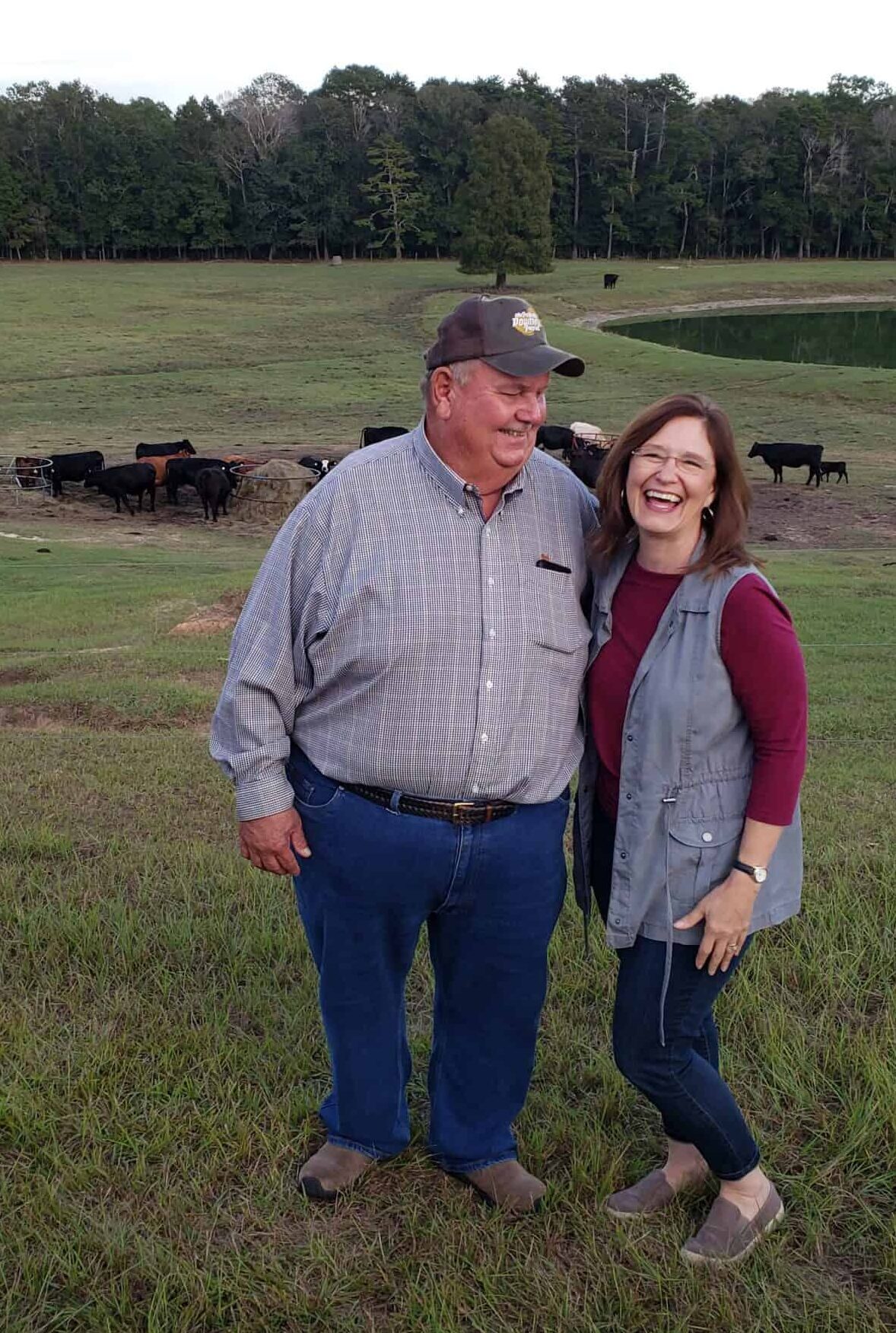 woman and man laughing with cows in back ground