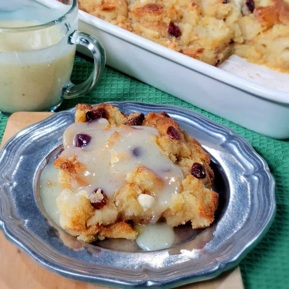 slice of bread pudding with cranberries white chocolate chips on a pewter plate 