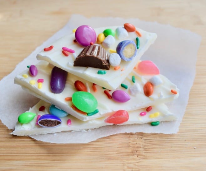 Three stacked pieces of white chocolate bark with Easter candy pressed into them placed on parchment paper