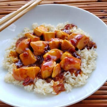 white plate of general tso's chicken on rice with chopsticks on side