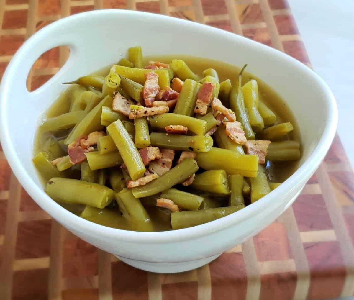 green beans with bacon in a white bowl on a checkered cutting board