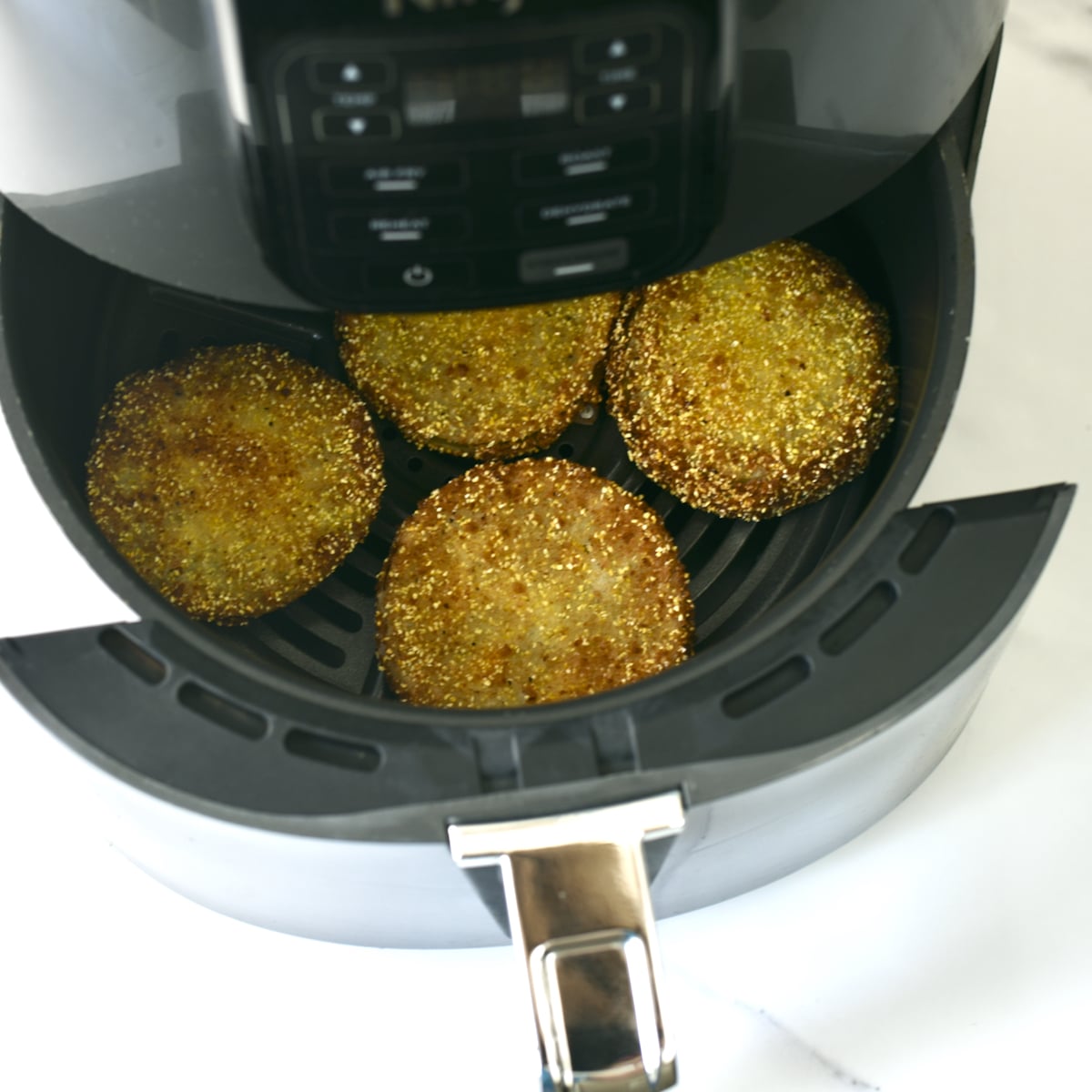 Fried green tomatoes in an open basket style air fryer.