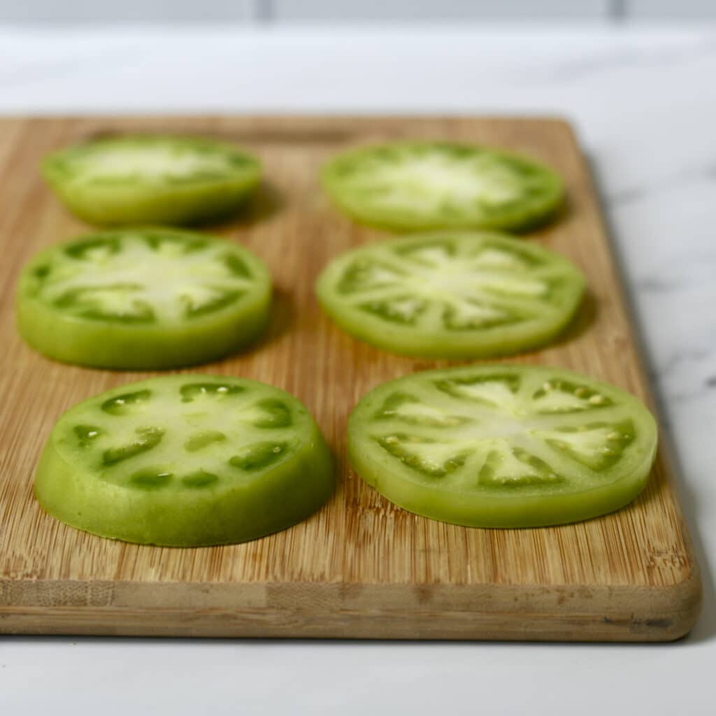 Thick and think slices of green tomatoes on bamboo cutting board.
