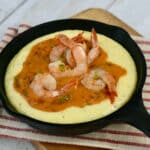 Small cast iron skillet filled with gouda cheese grits and topped with shrimp and tomato gravy.