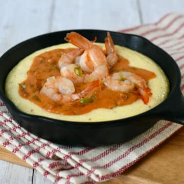 Small cast iron skillet filled with gouda cheese grits and topped with shrimp and tomato gravy.
