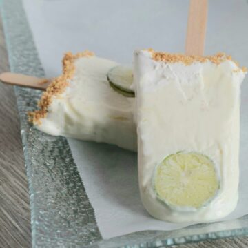 2 Key lime pie popsicles propped up against each other with slice of lime on the end