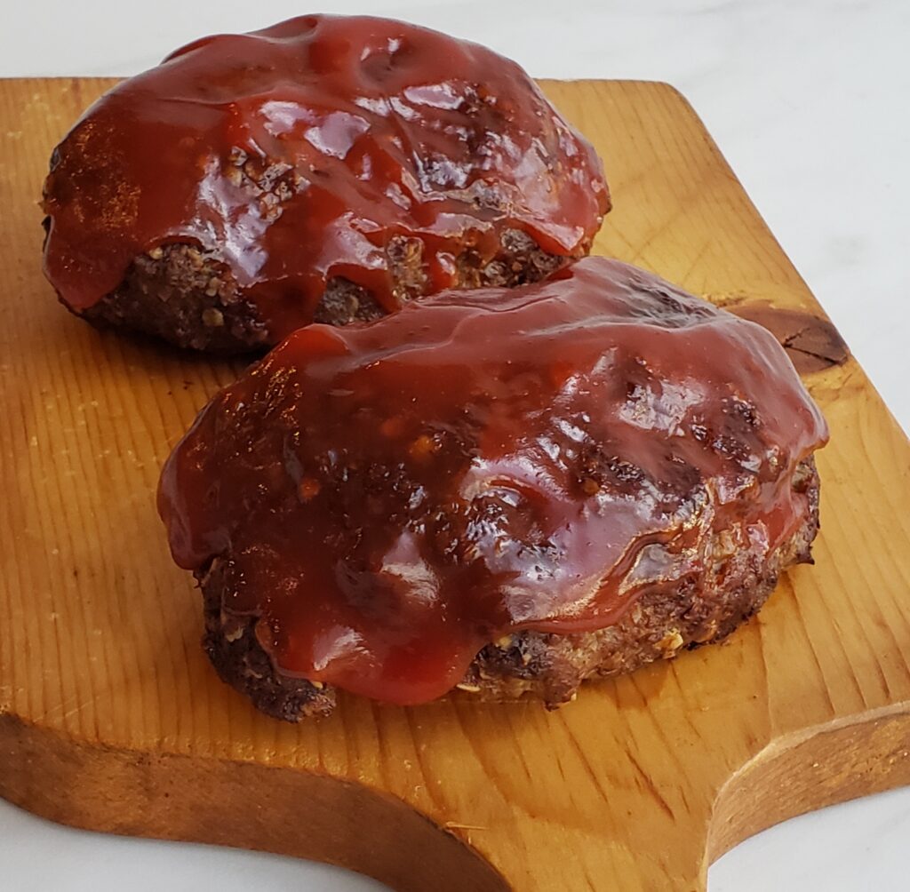 Two small meat loaves on a wooden cutting board with red sauce on top