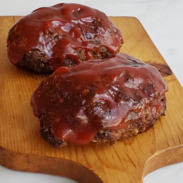 Two small meat loaves on a wooden cutting board with red sauce on top