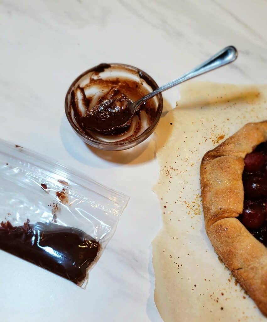 melted chocolate in a tiny bowl and zip loc bag with edge of a fruit pie in frame