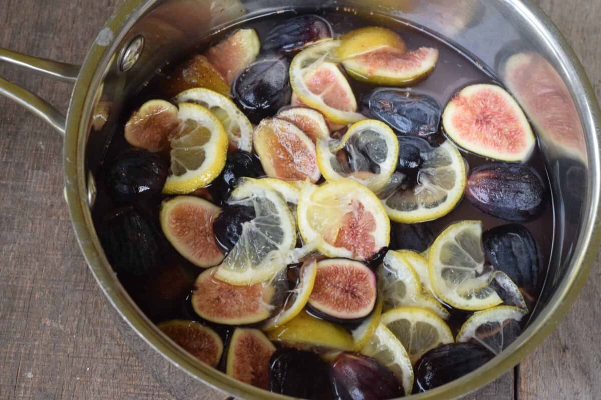 Saucepan full of sliced purple figs and lemons with water.