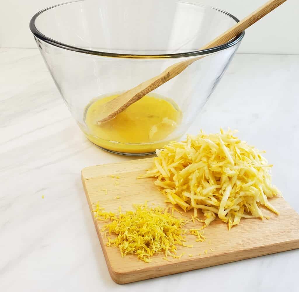 Beaten eggs in glass bowl; shredded yellow squash on wooden cutting board