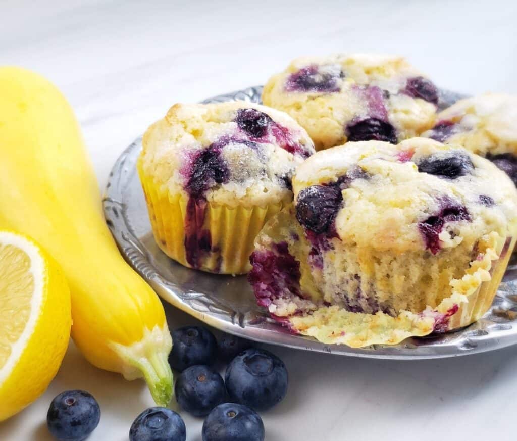 Lemon Blueberry Yellow Squash Muffins on pewter platter with squash and blueberries on surface