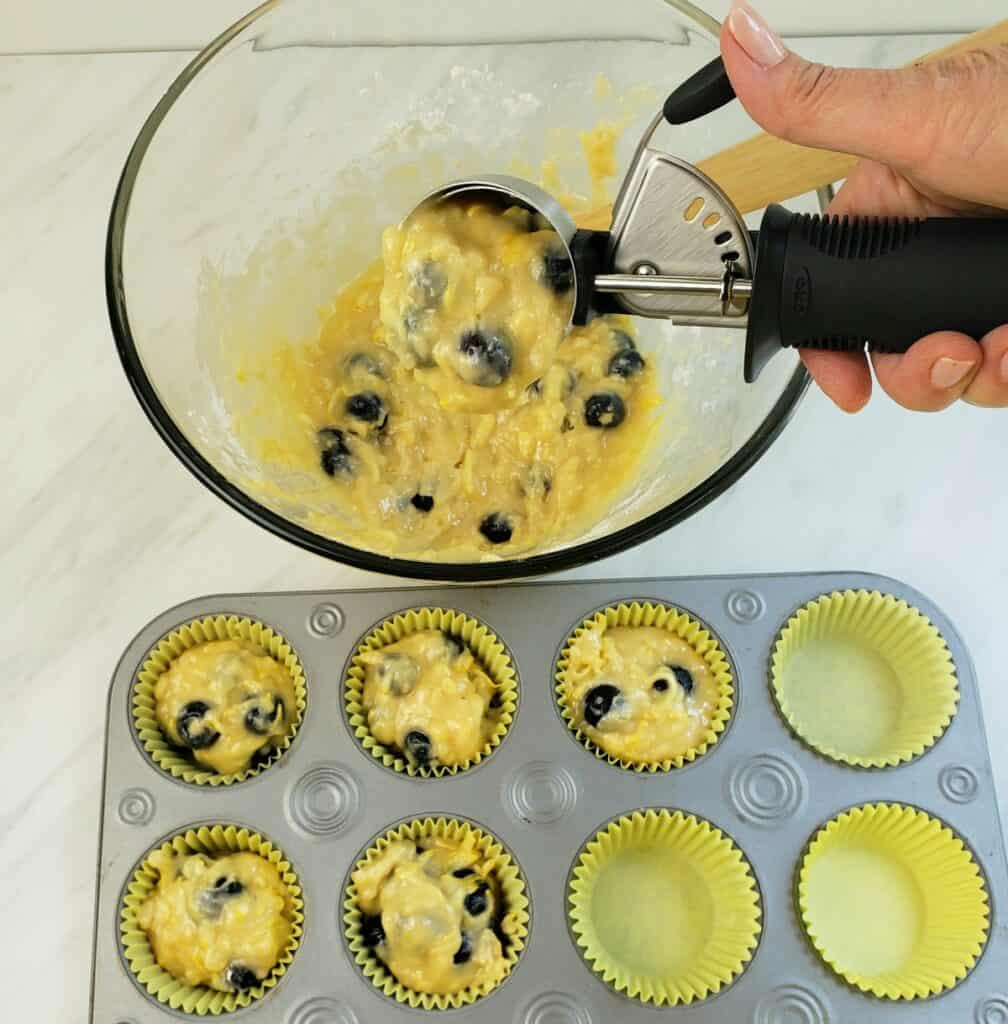 scooping lemon blueberry muffin batter in muffin cups with ice cream soop