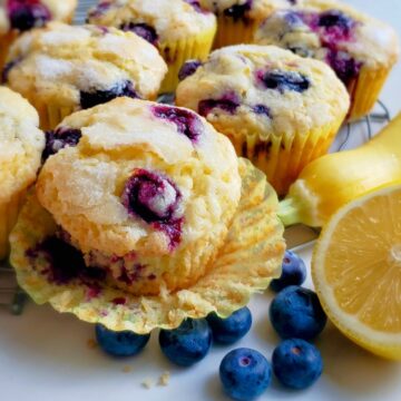 Lemon Blueberry Muffins with paper wrapper open next to a yellow squash and lemon with fresh blueberries.