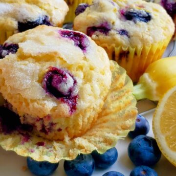Lemon Blueberry Muffins with paper wrapper open next to a yellow squash and lemon with fresh blueberries.