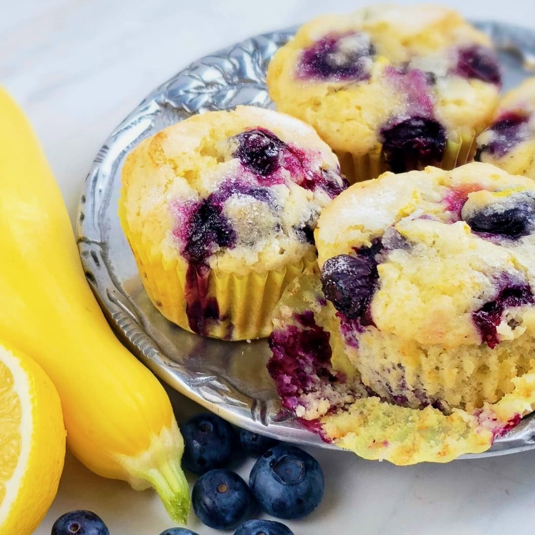 Lemon Blueberry Muffins on pewter plate next to a yellow squash and lemon with fresh blueberries.