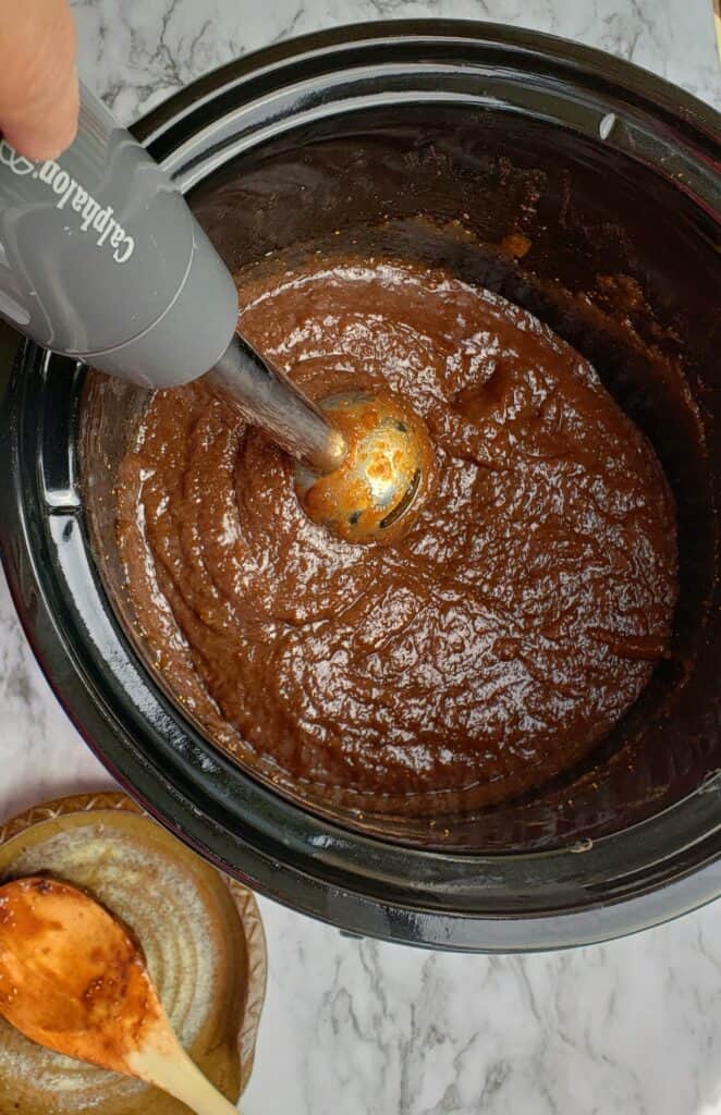 Immersion Blender in slow cooker crock of fig jam with pottery spoon rest on surface