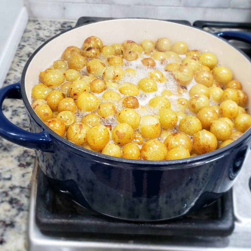 A blue dutch oven on a stovetop boiling scuppernong grapes for jelly.
