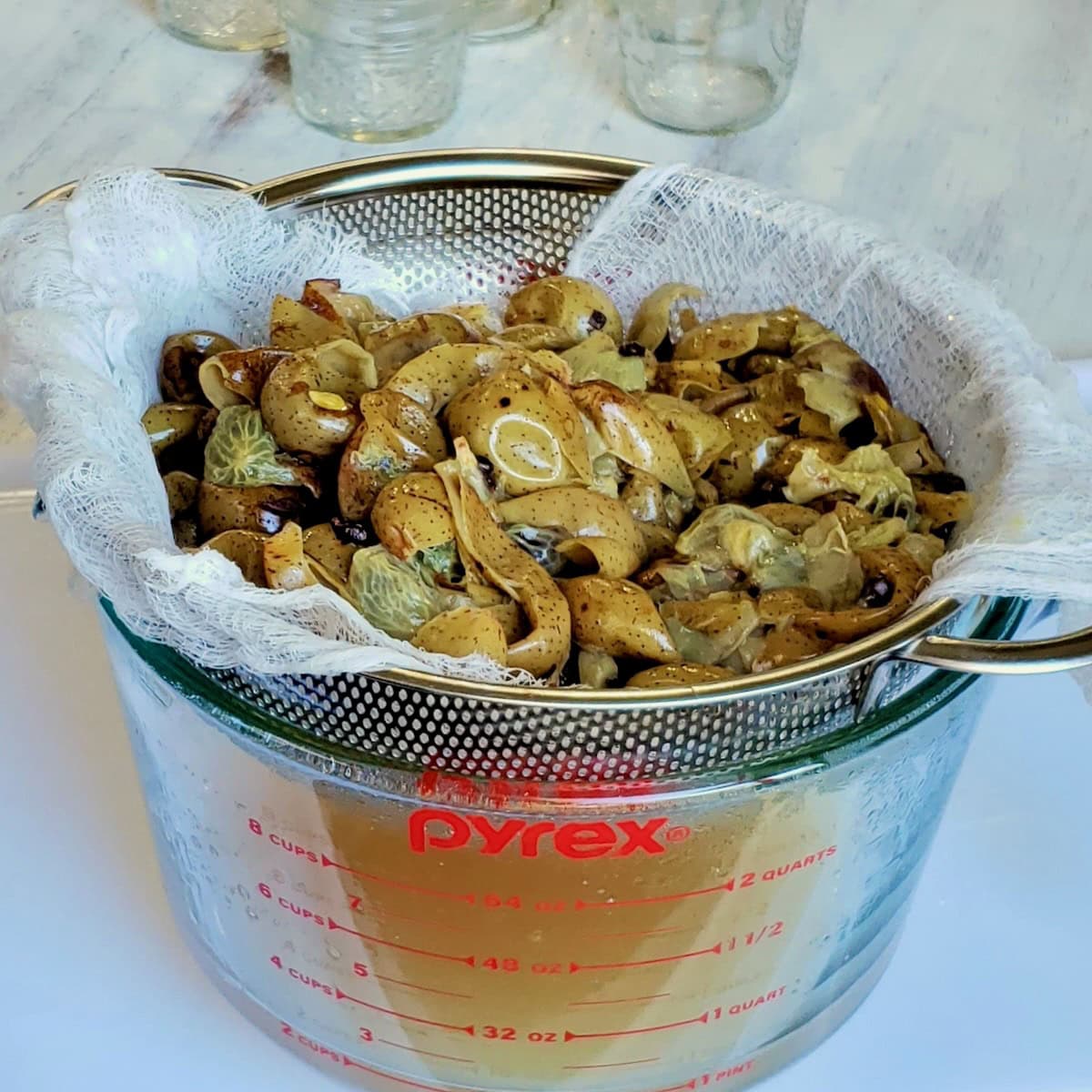 Cooked scuppernong grapes draining in a collander lined with cheesecloth.