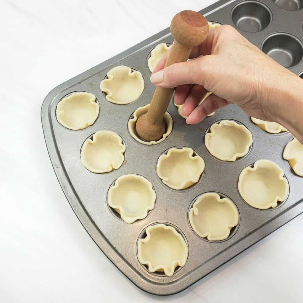 Pressing pie crust rounds into mini muffin pans with tart tamper