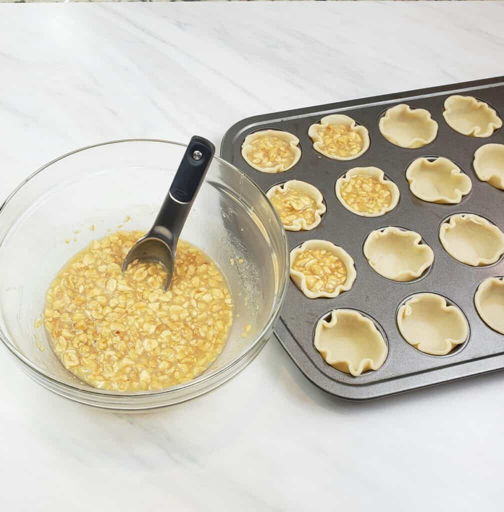 mini peanut pies in muffin pans before baking with bowl of filling