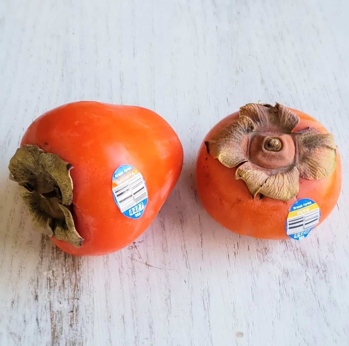 Two kinds of persimmons with labels on them on white surface.h