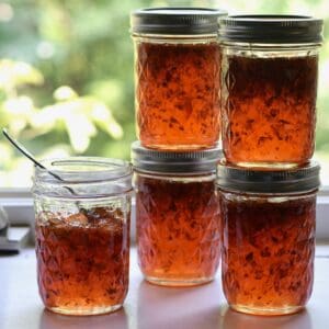 Jars of jalapeno pepper jelly stacked in window.