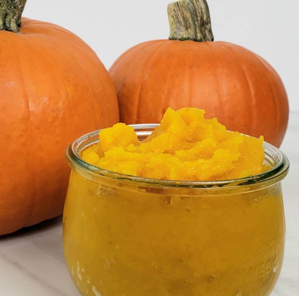 pumpkin puree in a glass dish with 2 pumpkins in background