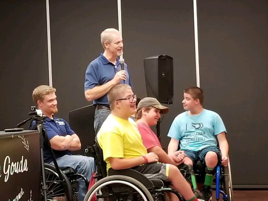 4 boys in wheelchairs, man with mic