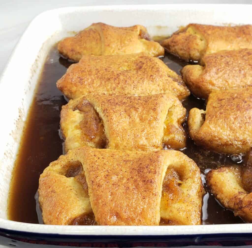 Baked crescent roll dough filled with pumpkin filling and brown sugar sauce in square dish