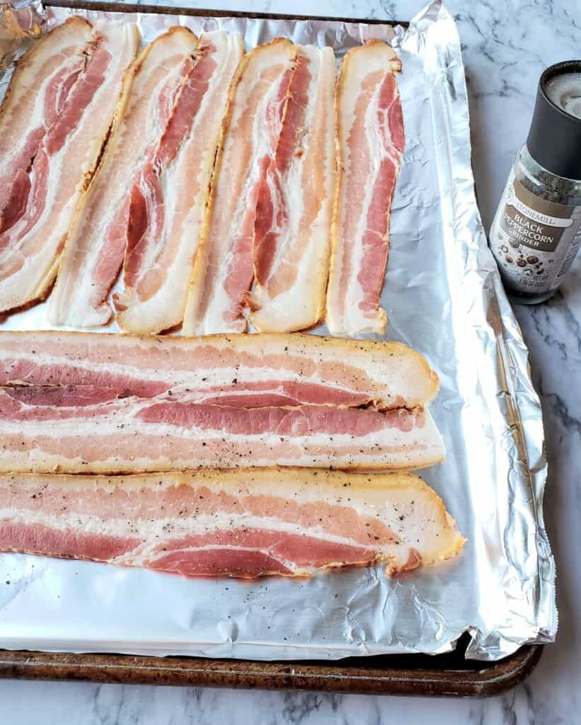 Thick cut bacon on a foiled line sheet pan with pepper grinder to the side