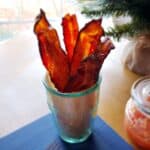 Candied bacon stacked upright in a green vase with a Christmas tree branch in background